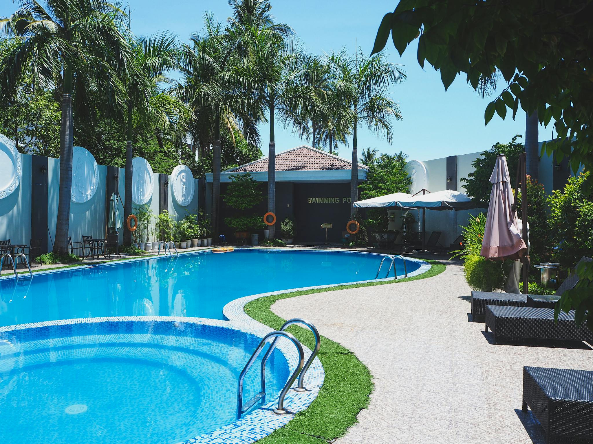 outdoor swimming pool with sunbeds on territory of tropical hotel with green palm trees against cloudless blue sky 5746250